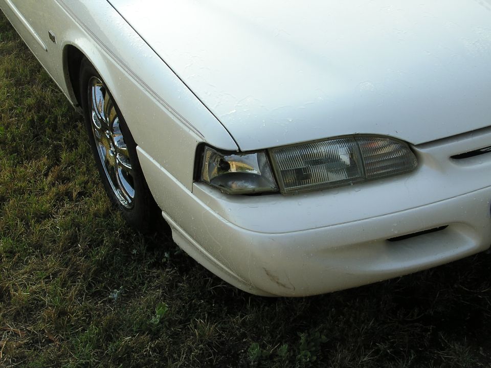Front right corner of white Ford Thunderbird with damaged headlight lens and chrome wheel, parked on grass