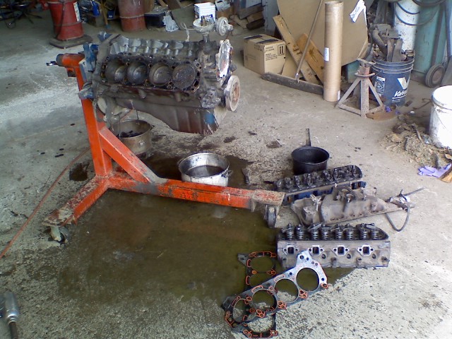 Engine block on an orange engine stand with disassembled parts on the floor