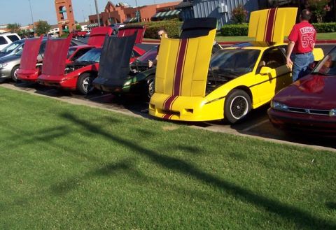 1988 Pontiac Fiero - Several Pontiac Fieros are parked in a row with their hoods open, displaying their engines.