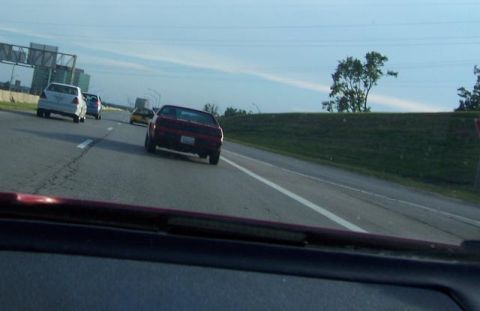 1988 Pontiac Fiero - A red sports car is seen from behind on a highway, with other vehicles in traffic.