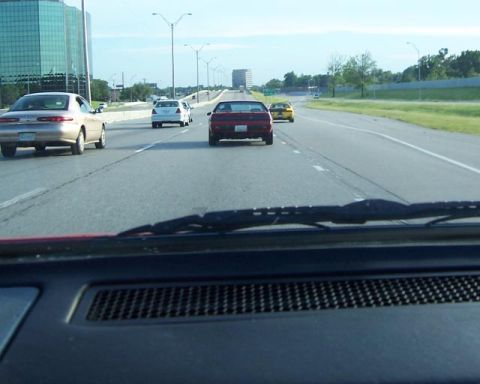 1988 Pontiac Fiero - A red 1988 Pontiac Fiero is seen driving on a highway, with other vehicles around it.