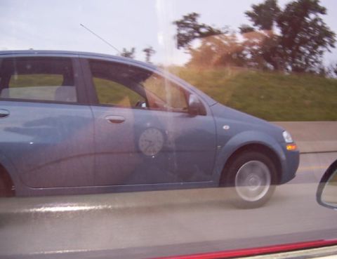 1988 Pontiac Fiero - A blue hatchback with a clock on its door is seen driving on a highway.
