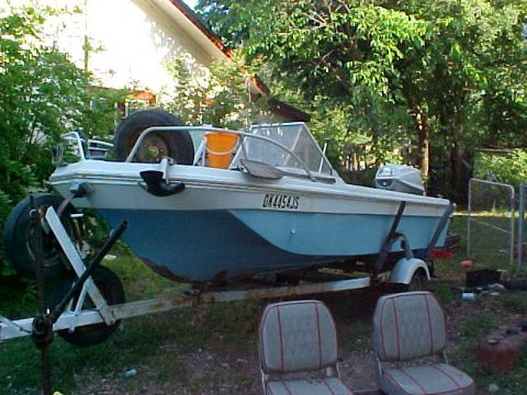 1987 Ford Bronco - A boat sits on a trailer, its blue hull contrasting with the white deck, surrounded by greenery.