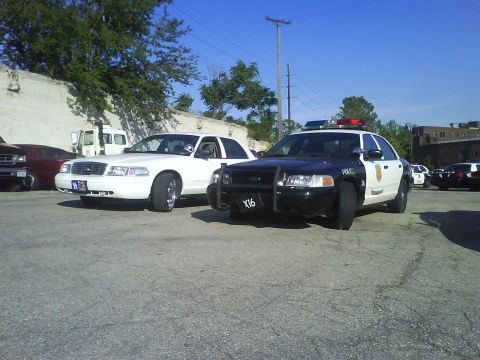 2003 Ford Crown Victoria - Two Ford Crown Victoria police cruisers are parked side-by-side on a sunny day.