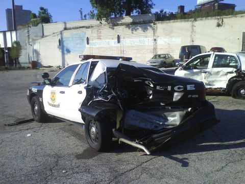 2003 Ford Crown Victoria - Two heavily damaged police cars are parked side-by-side after an apparent collision.