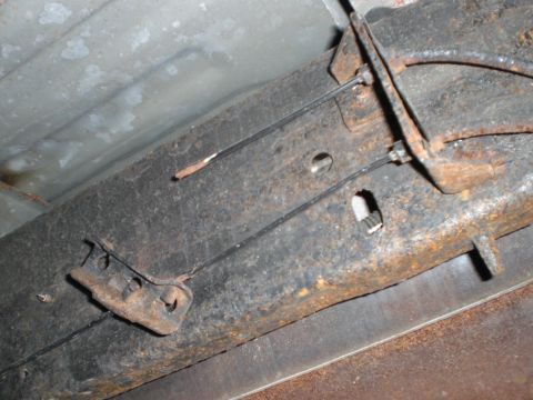 1995 Ford F-150 - Close-up view of the emergency brake cables and mounting hardware on a heavily rusted vehicle frame.
