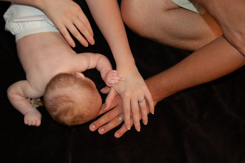 Baby's hand touching adult's hand, with other family members present.