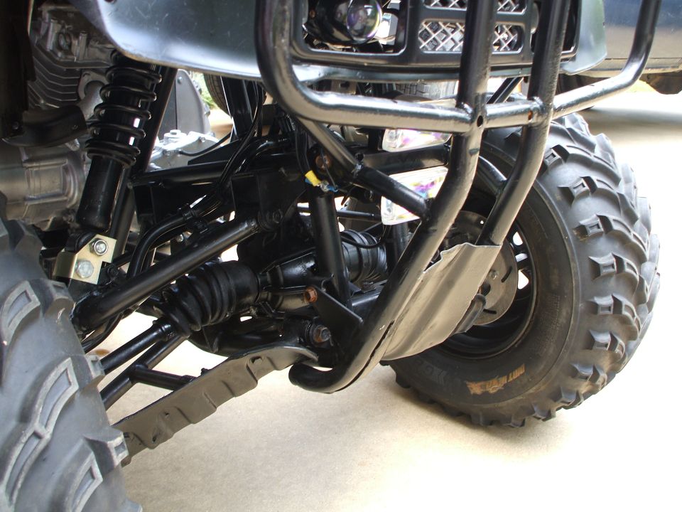 Underside front suspension of a black ATV with shock, A-arms, CV boot, and knobby tire