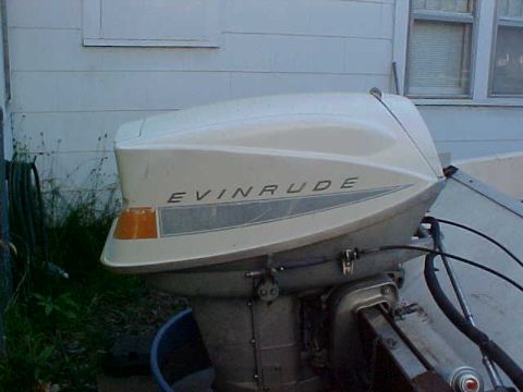 1987 Ford Bronco - An Evinrude outboard motor is mounted on the back of a boat, with a building in the background.