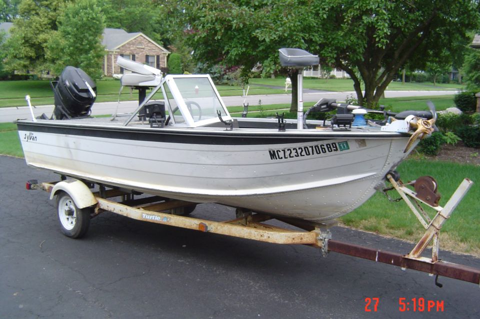 White Sylvan aluminum fishing boat with outboard motor on a trailer in a driveway