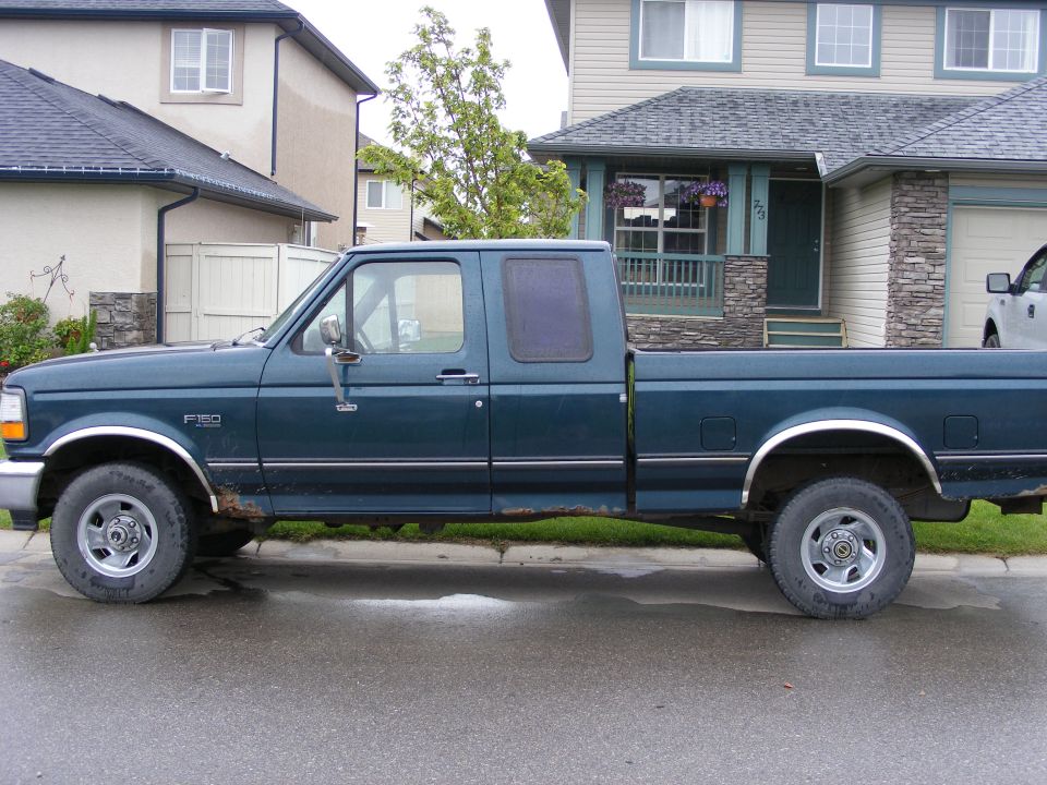 Side profile of a teal extended-cab pickup truck parked on a residential street