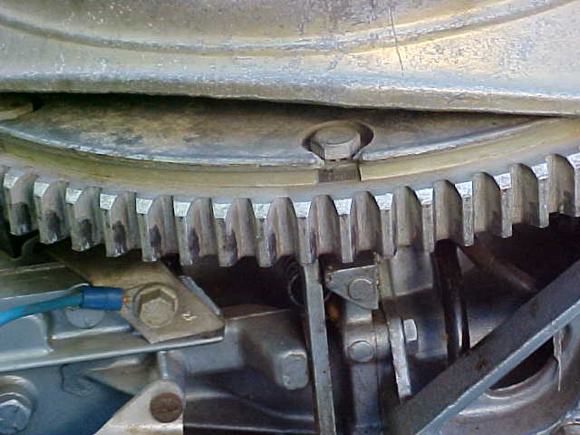 Close-up of a toothed metal gear and engine components with a blue wire