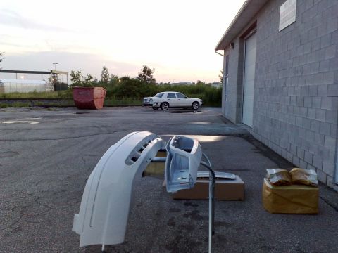 2003 Ford Crown Victoria - Two white car bumper parts are laid out on the asphalt in front of a gray cinder block building. A white sedan is parked in the background…