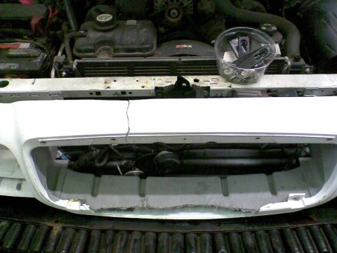 2003 Ford Crown Victoria - A white front bumper cover and grille removed from a car and laid on a truck bed liner, showing a cracked upper edge and torn mounting tabs…