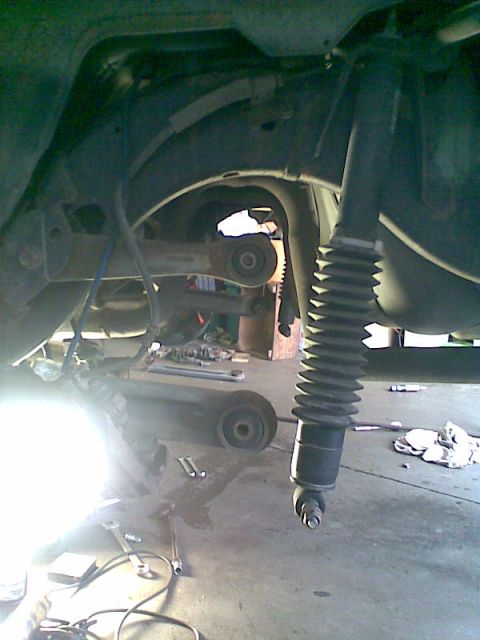 2003 Ford Crown Victoria - Underbody shot of a car's rear suspension with the axle dropped and the wheel removed, showing a new black shock absorber with a ribbed rub…
