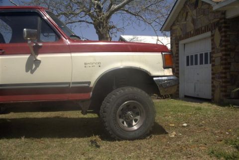 1987 Ford Bronco - This two-tone Ford Bronco is parked on a grassy area next to a brick garage with a white door.