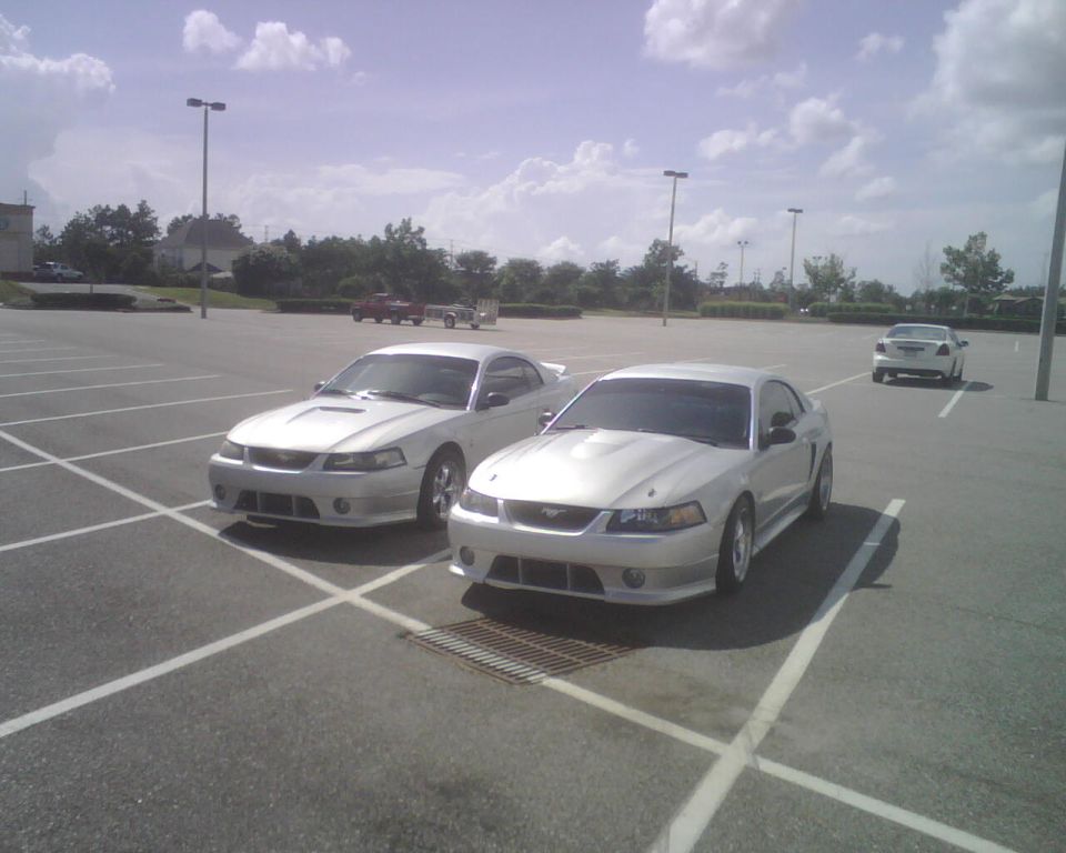 Two silver 1999 Ford Mustangs parked in a lot, front 3/4 view