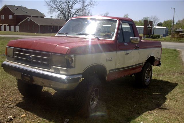 Red and white pickup truck with lifted suspension and large tires