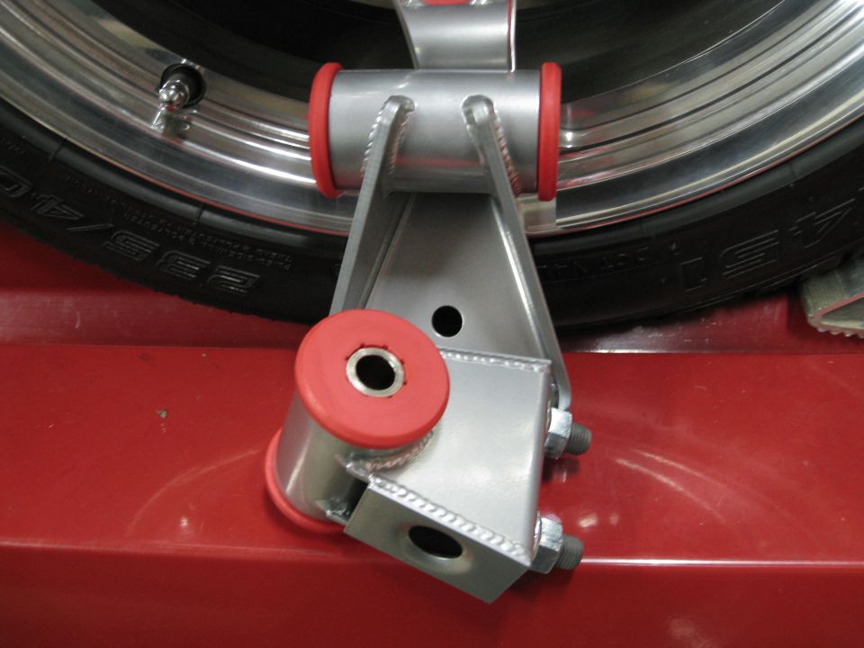 Aftermarket suspension component with red polyurethane bushings next to a tire and wheel