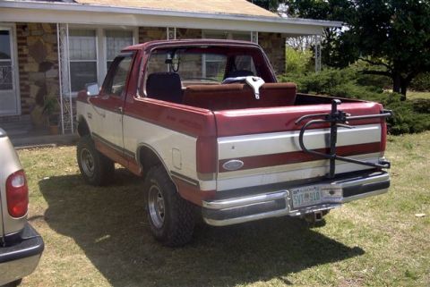 1987 Ford Bronco - This two-tone Ford Bronco is parked in front of a house with a spare tire carrier mounted on the rear.