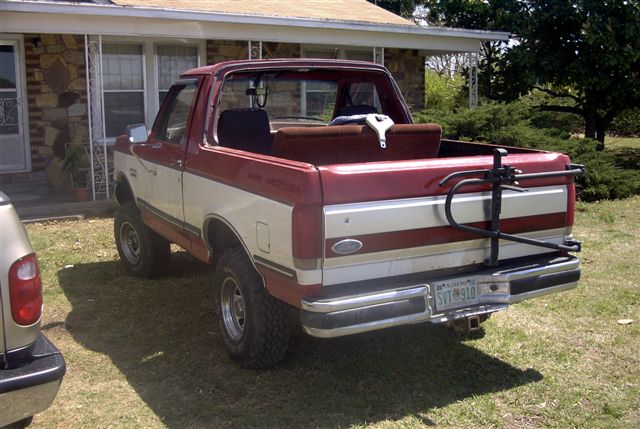Two-tone red and white Ford Bronco parked in front of a house. Spare tire carrier on the back