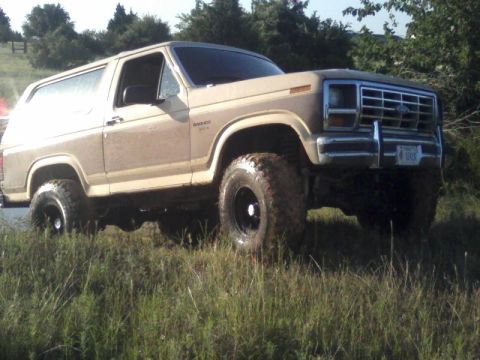 1986 Ford Bronco - This lifted Ford Bronco is shown from a three-quarter front angle, with its front grille and tires visible.