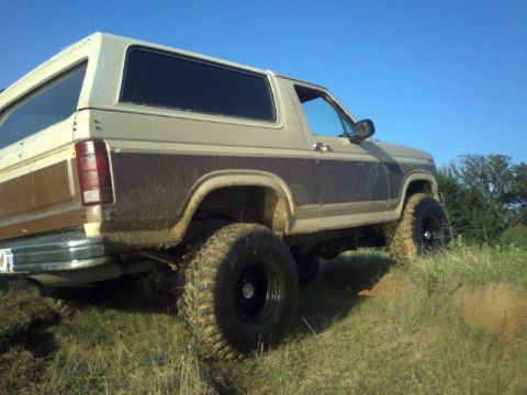 1986 Ford Bronco - This lifted 1980s Ford Bronco is shown from the rear 3/4 angle while navigating an off-road trail.