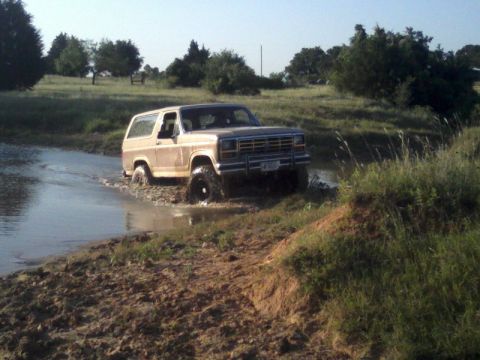 1986 Ford Bronco - This 1980s Ford Bronco is navigating through a muddy, watery terrain under a clear sky.