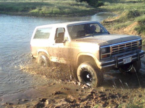 1986 Ford Bronco - This 1986 Ford Bronco is navigating a muddy off-road trail with water obstacles.