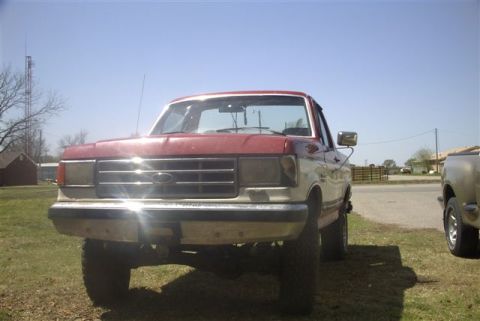 1987 Ford Bronco - A red and white Ford truck is parked on a grassy area under a clear blue sky.