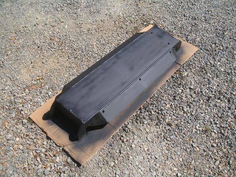 1989 Ford Bronco - A black metal tcase skid plate is shown from a high angle, placed on cardboard on a gravel surface.