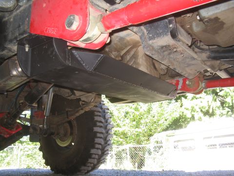 1989 Ford Bronco - Custom transfer case skid plate installed on a vehicle, red suspension components and a large off-road tire visible.
