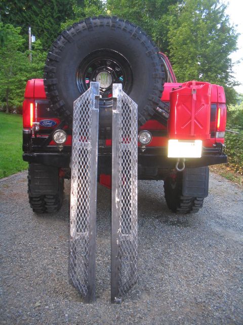 1989 Ford Bronco - Rear view of a red Ford Bronco with a spare tire, jerry can, and two metal ramps.
