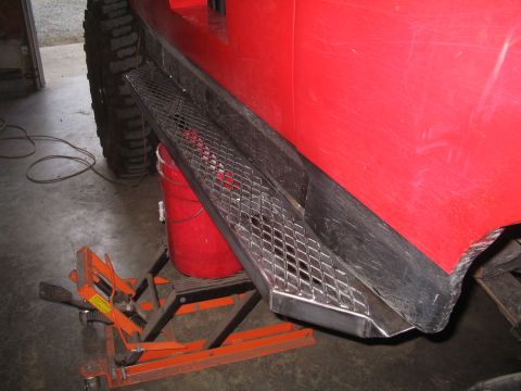 1989 Ford Bronco - Custom diamond plate rock sliders are mounted to the side of a red vehicle in a garage.