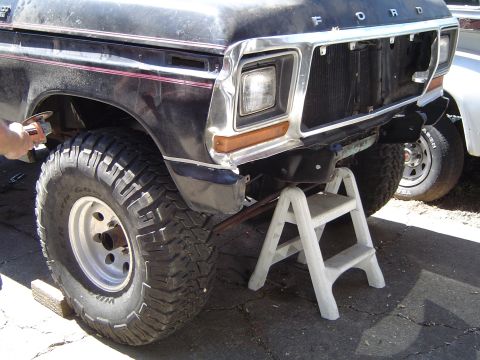 1979 Ford Bronco - Close-up of a 1979 Ford Bronco's front end being worked on, with a second vehicle visible to the side.