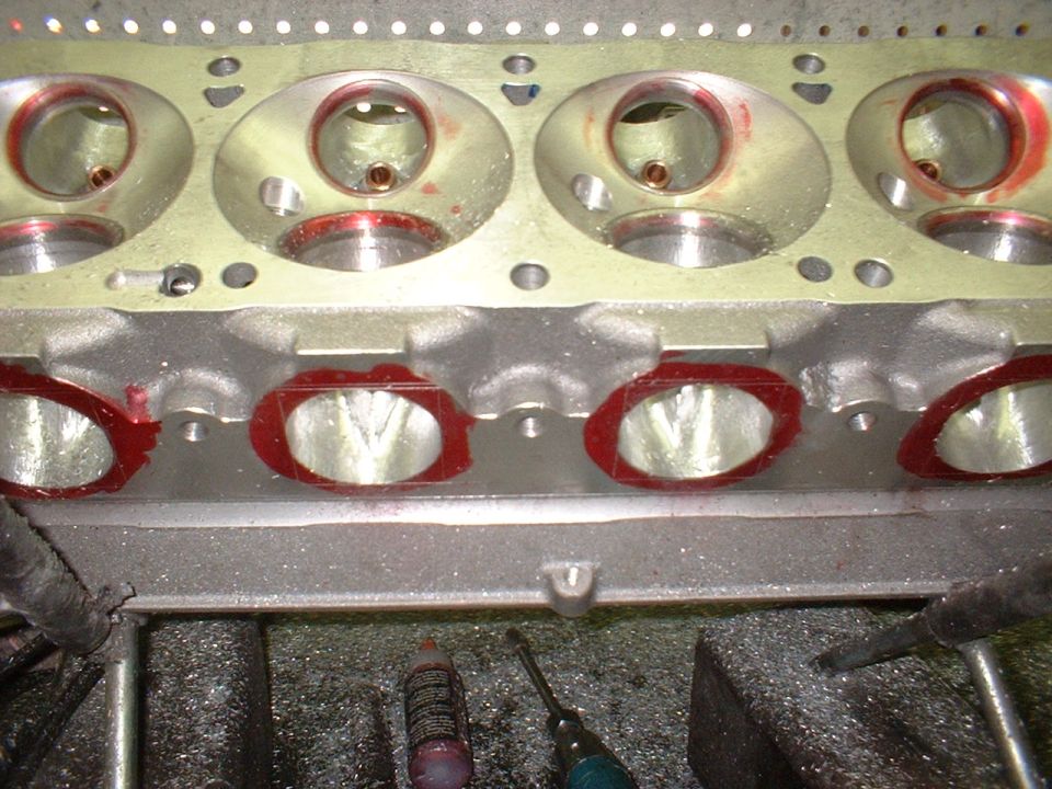 Aluminum cylinder head on a workbench showing combustion chambers and ports marked with red dye