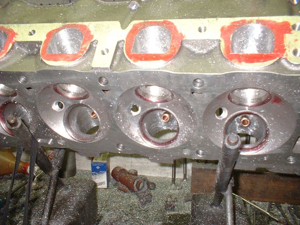 Machined V8 cylinder head close-up with bronze valve guides and red-outlined ports