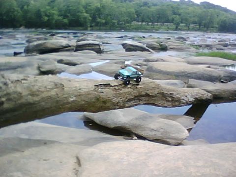 1996 Ford Bronco - A small toy truck is positioned on a large rock in a shallow river with trees lining the far bank.