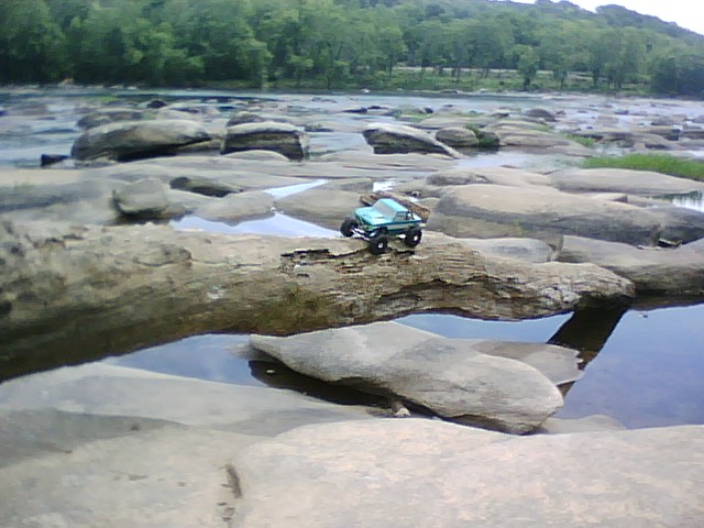toy truck on a rock in a riverbed with trees in the background