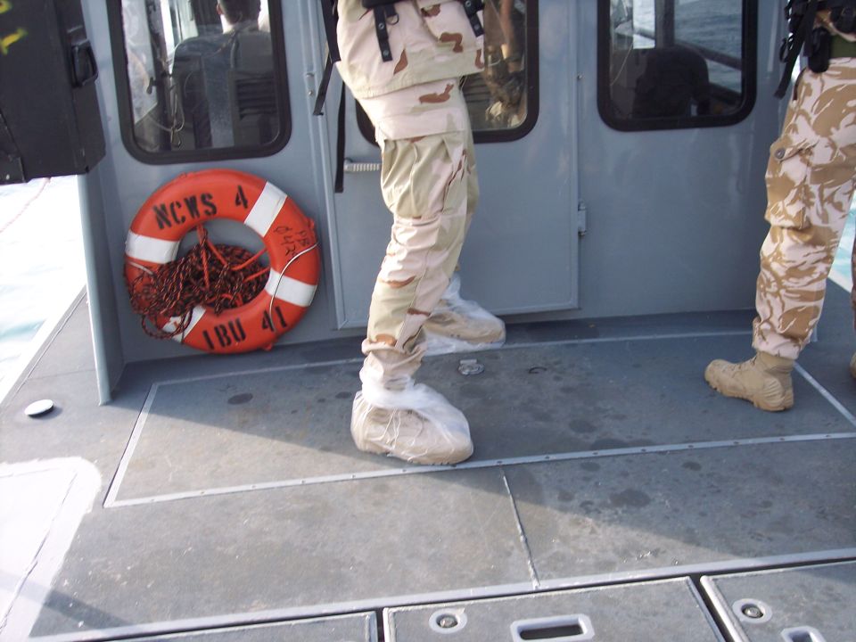 Crew in desert camouflage on the deck of a gray patrol boat with life ring