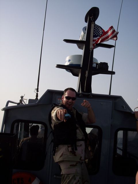1981 Kenworth W900A - A man in military-style uniform gestures assertively while standing on a boat, with an American flag visible.