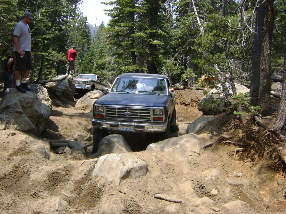 Blue lifted Ford Bronco picking through a rocky trail with onlookers