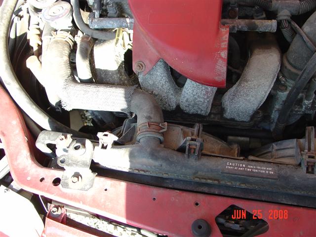Engine bay showing radiator, hoses, and engine components. Text on radiator reads 'CAUTION: REAR WINDOW MAY START AT ANY TIME IGNITION IS ON'