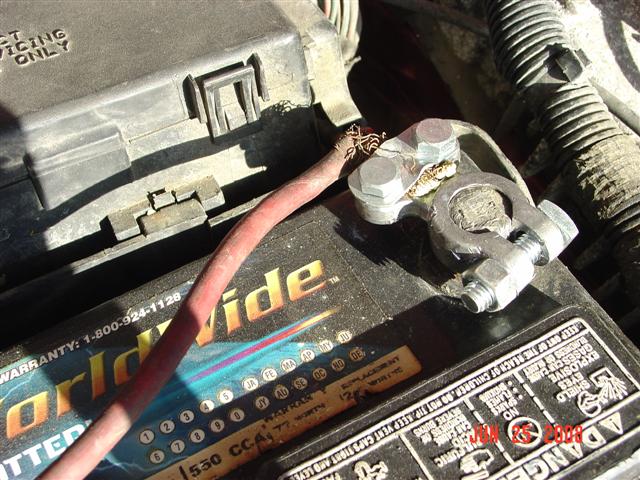 Car battery with red cable connected to terminal. Fuse box lid is visible