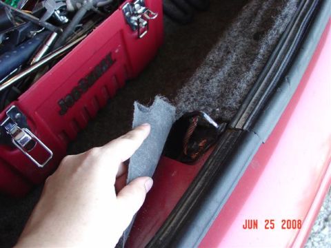 1997 Dodge Neon - A hand pulls at insulation in the trunk of a red car, next to a red toolbox.