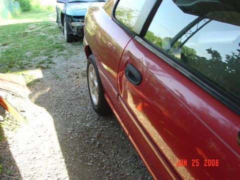 1997 Dodge Neon - Two cars are parked on a gravel driveway. The red car is in the foreground, and a blue car is behind it.