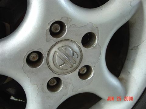 1997 Dodge Neon - A close-up view of a damaged alloy wheel with a logo on its center cap.