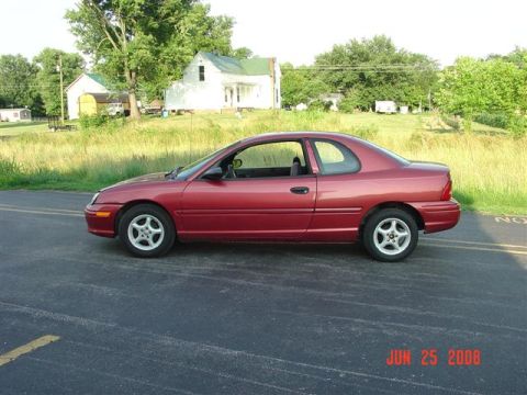 1997 Dodge Neon - A red 1997 Dodge Neon coupe is seen from the side on a paved road with houses in the background.