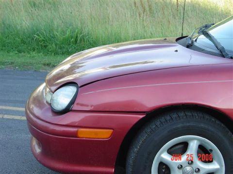 1997 Dodge Neon - The front quarter panel and headlight of a red 1997 Dodge Neon are visible, with a thin white stripe along the fender.