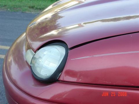 1997 Dodge Neon - Close-up of the front passenger side headlight and hood of a red 1997 Dodge Neon.